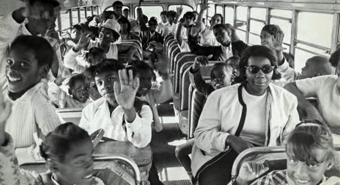 several children waving and schoolteacher on a bus
