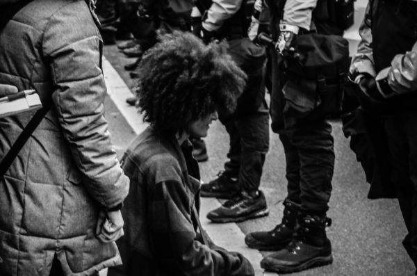 person kneeling in front of police in riot gear