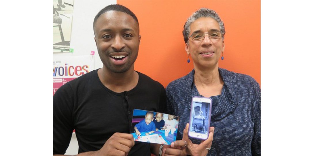 two people posing for photograph holding an old picture and a cell phone