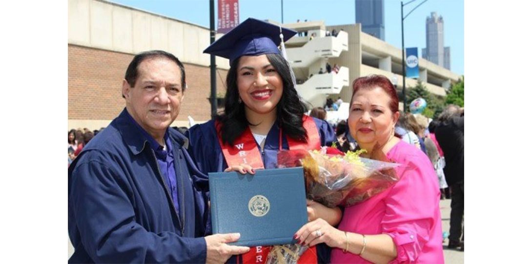 student in navy cap and gown holding flowers and diploma with parents on either side