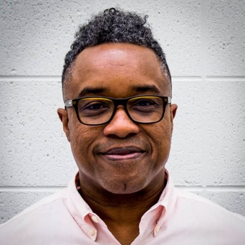 A person stands before a white brick wall to be photographed