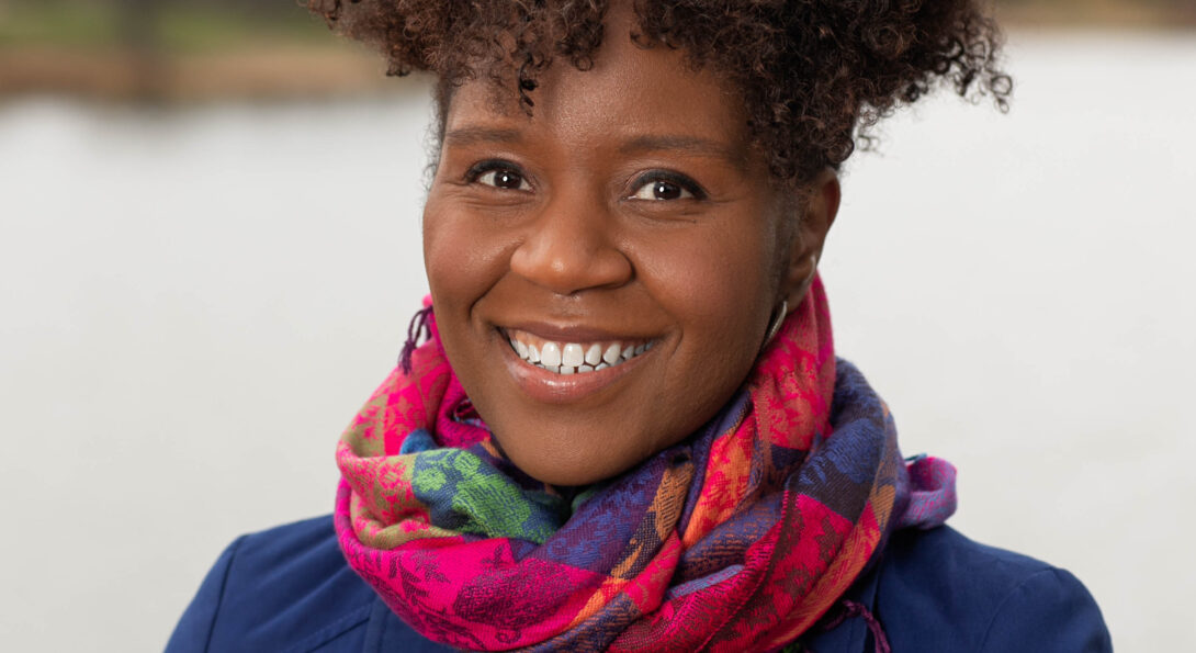 Portrait of a Black woman smiling to the camera against a blurred background.