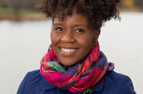Portrait of a Black woman smiling to the camera against a blurred background.