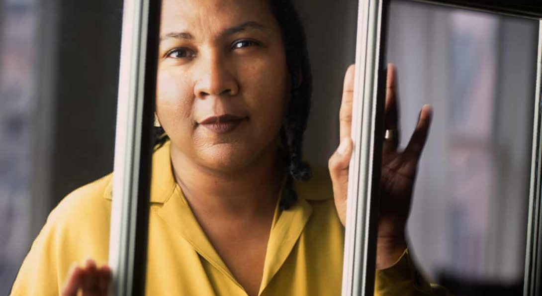 black woman in yellow collared shirt with hands pressed on window