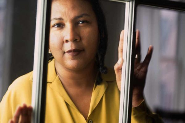 black woman in yellow collared shirt with hands pressed on window