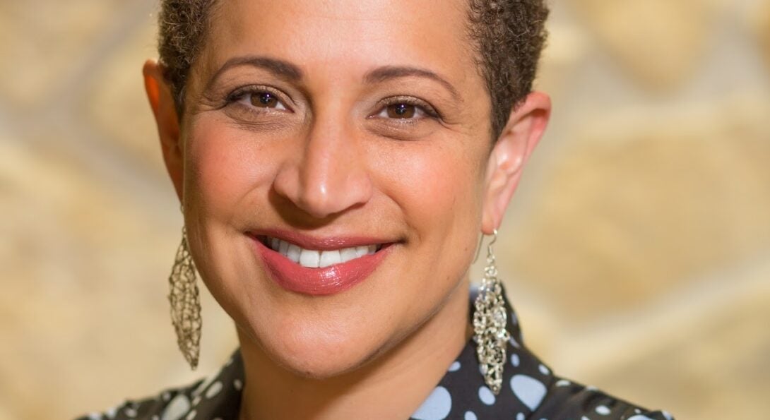 person wearing a polka dot shirt and gold jewelry smiles at the camera