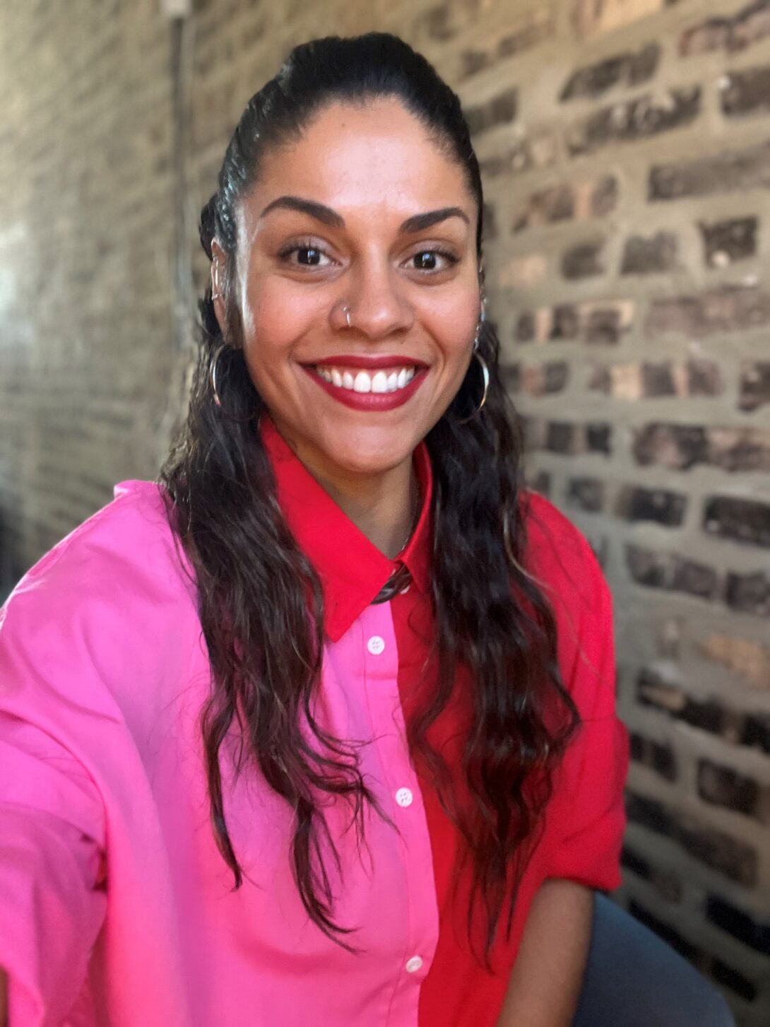 woman standing in front of a brick wall wearing a pink and red shirt