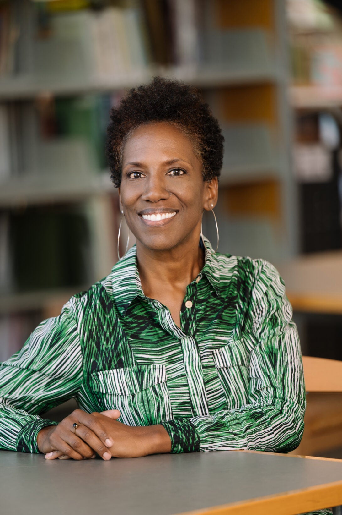 woman wearing a green patterned shirt sitting at a table in a library