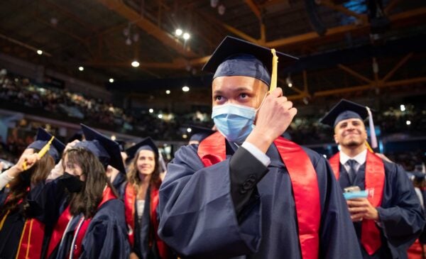 person wearing graduation regalia and a mask moving their tassle