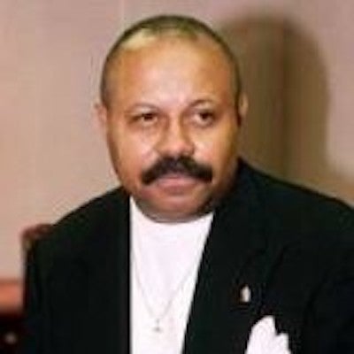 man in black jacket with white undershirt with mustache looking at camera