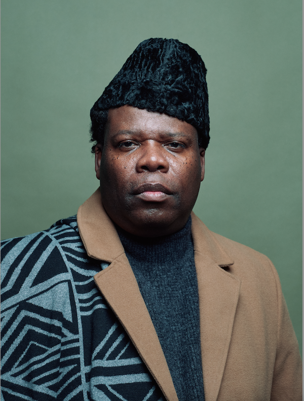 man with black hat and brown jacket looking at camera