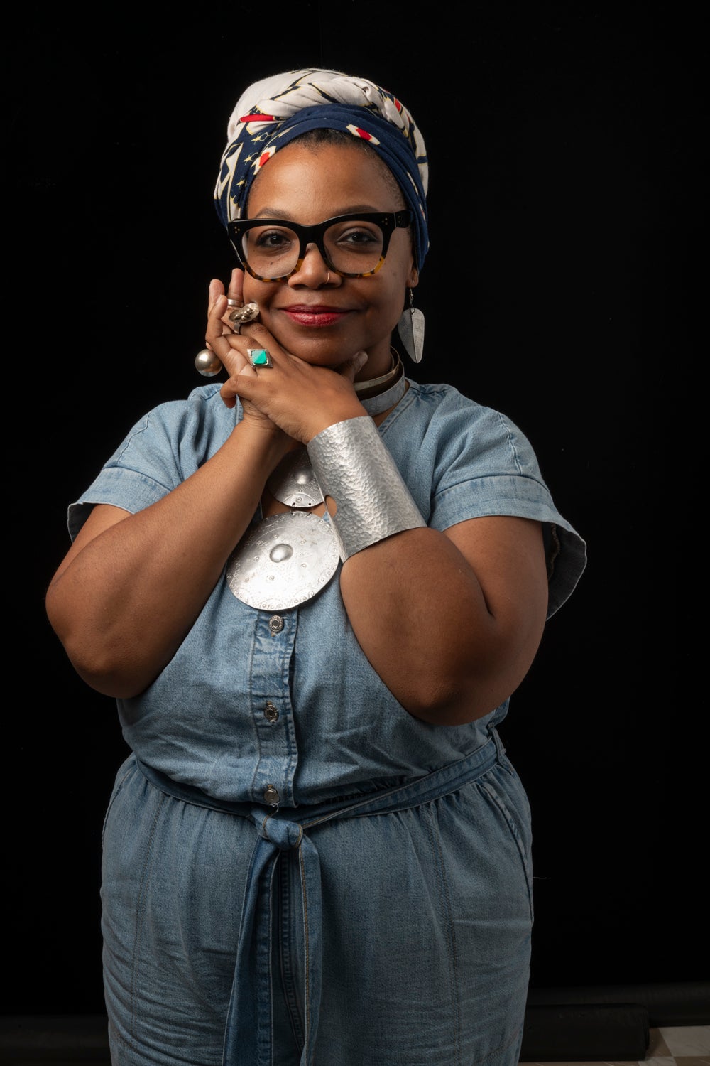 standing woman wit hair wrap and glasses smiling at camera