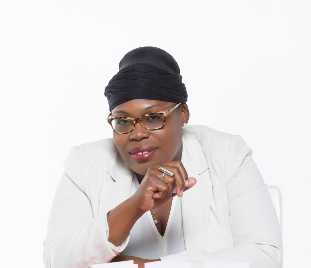 woman wearing white jacket and shirt with glasses and head wrap looking at camera